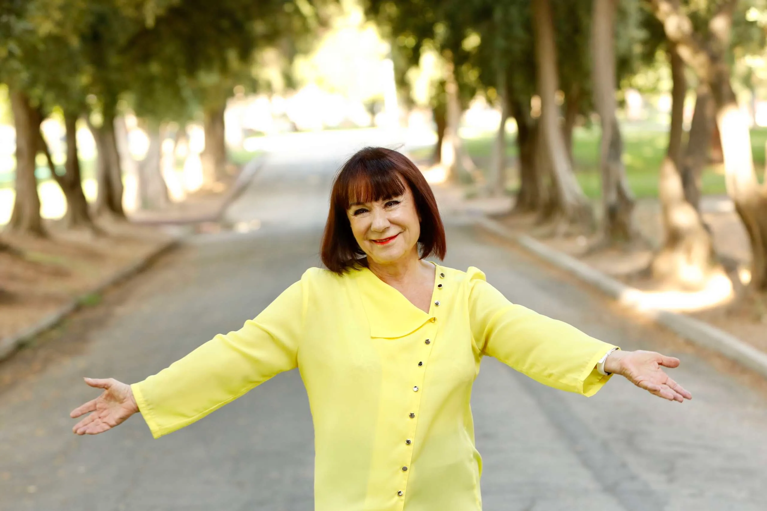 Hypnotherapist-Coach-Evie-Sullivan, with-open-arms,-wearing-a-bright-yellow-outfit.