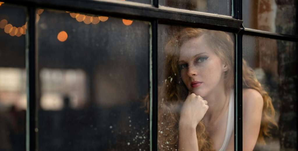 Woman standing by a sunlit window, reflecting quietly before beginning a guided hypnotherapy session for emotional healing.