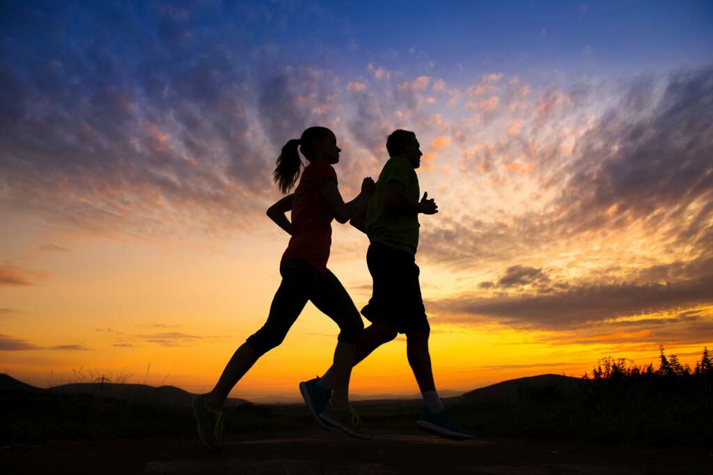 Silhouette of two people running at sunset, representing the harmony between initial motivation and steady commitment in personal growth.