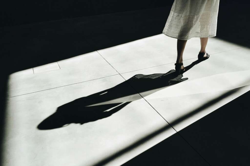 Person standing in sunlight casting a long shadow on the floor, symbolizing the shadow of addiction and the hidden fears beneath everyday life.
